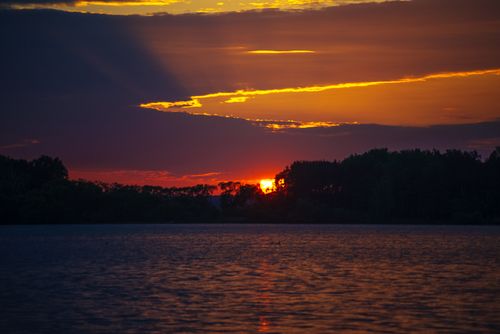 Free A striking sunset over a serene lake, with silhouettes of trees creating a dramatic reflection. Stock Photo