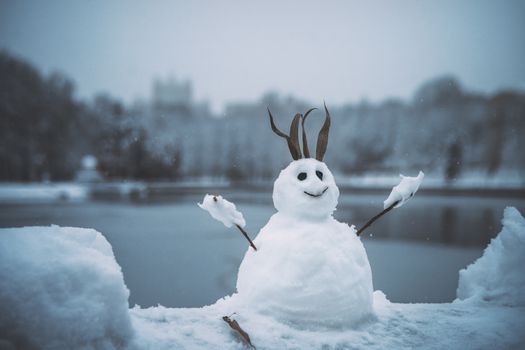 Cheerful snowman with stick arms by a frozen lake on a winter day.