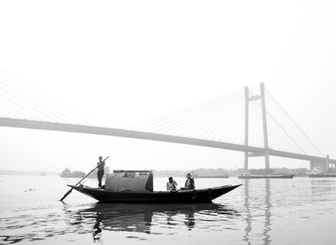A serene black and white image of a boat on the Hooghly River with Vidyasagar Setu in the background.