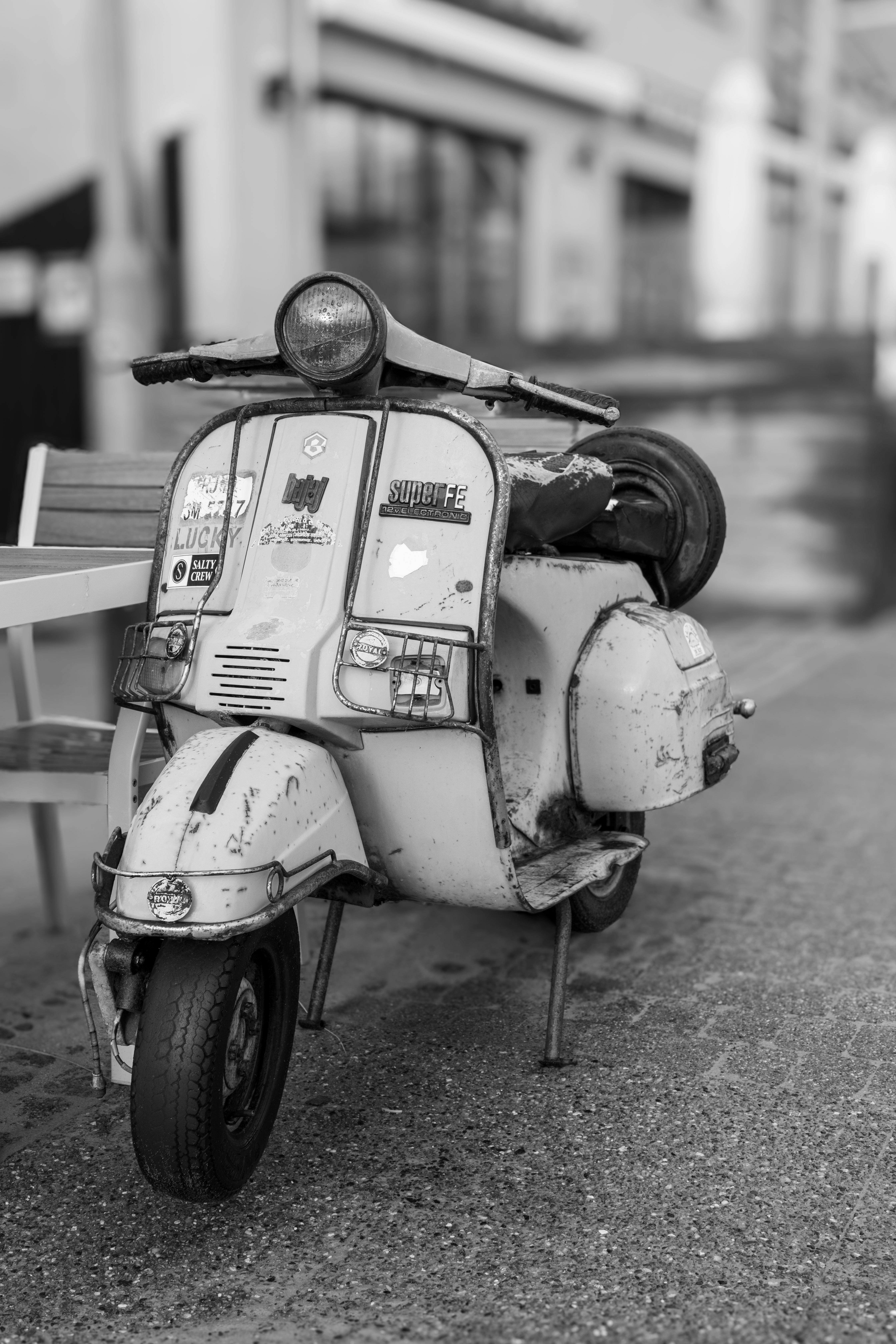 Free Black and white image of a vintage scooter parked on a city street. Stock Photo