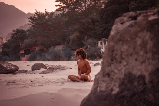 A teenager sits in meditation on a sandy beach in Rishikesh, India, embracing tranquility.