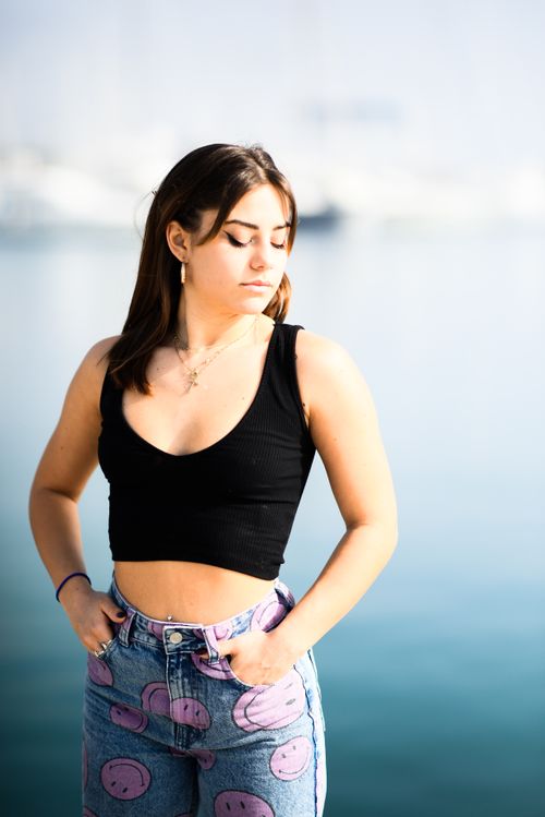 Free A young woman in a crop top stands by the sea, enjoying the sunlight. Stock Photo