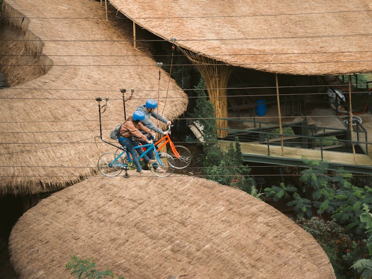 Woman And Man Riding Bikes On Lines Over Thatched Roofs