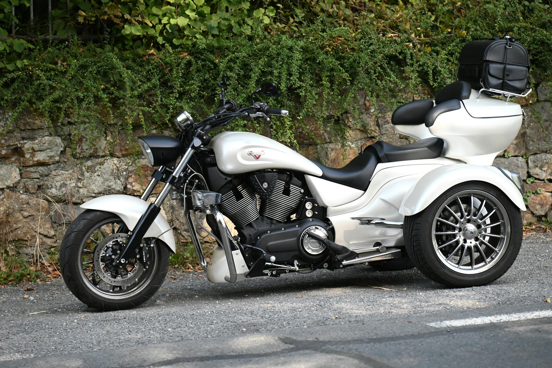 A stylish white trike motorcycle parked on a scenic road with lush greenery backdrop.