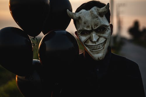 Man Standing Outside in a Scary Halloween Mask and Holding Black Balloons 