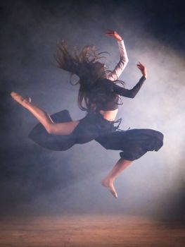 A dancer midair performing a dramatic leap with billowing fabric and a smoky background.