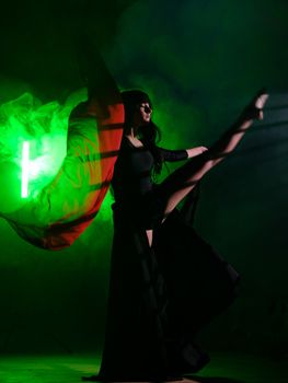 A dancer strikes a dramatic pose with flowing fabric and a smoky green background.