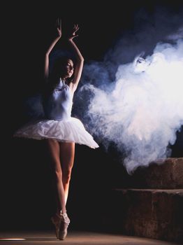 A graceful ballet dancer performs on stage surrounded by dramatic smoke effects.