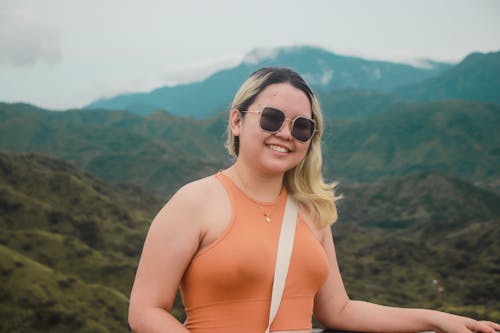 Smiling Woman in Orange Top Posing Against Mountains
