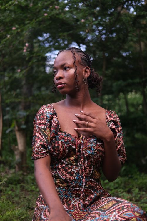 Free Portrait of a young woman in a patterned dress surrounded by lush greenery. Stock Photo
