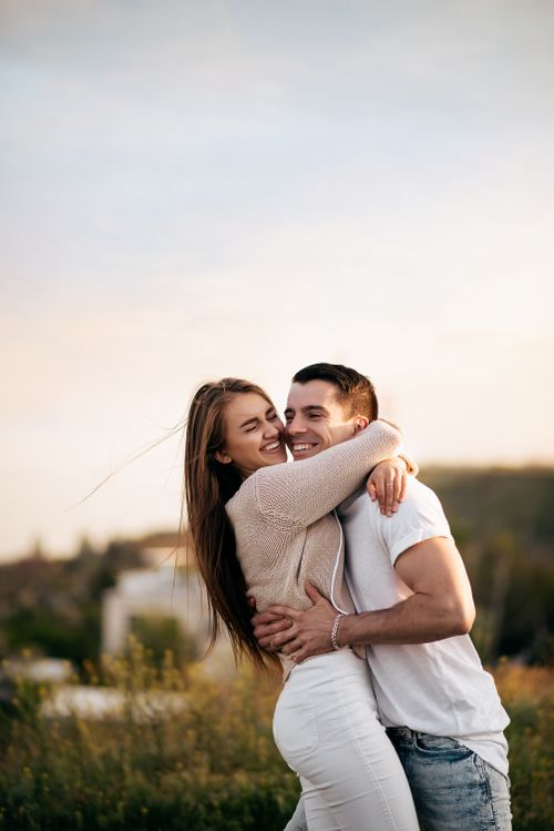 Free A happy young couple embraces outdoors, surrounded by nature's warmth and sunlight. Stock Photo