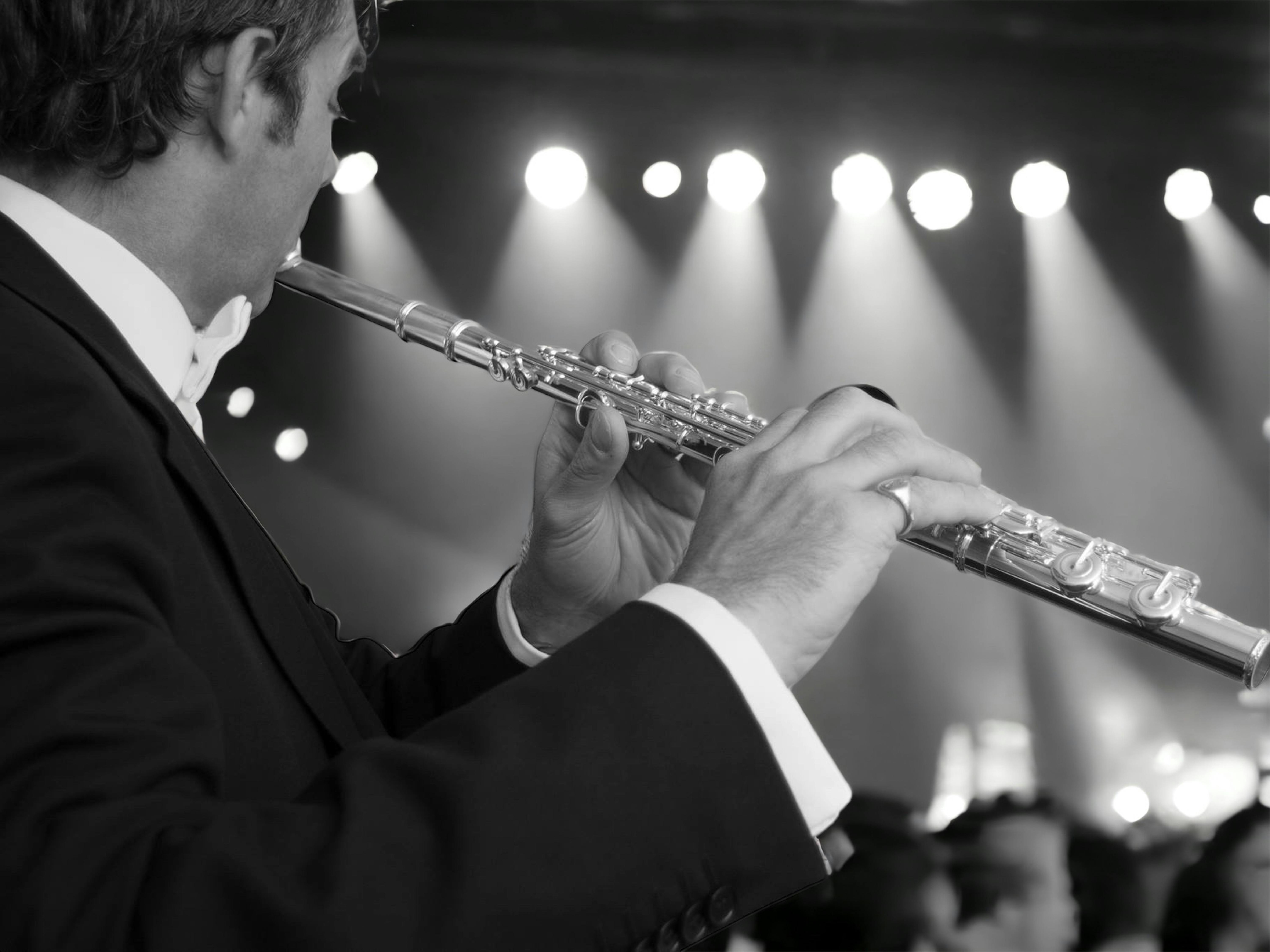 A musician in a suit playing flute in a concert setting, captured in black and white.