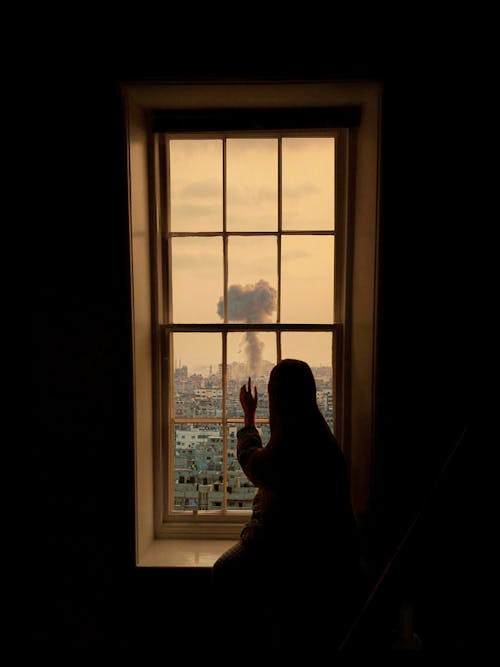 Silhouette of a Woman Sitting near a Window and Looking at the City