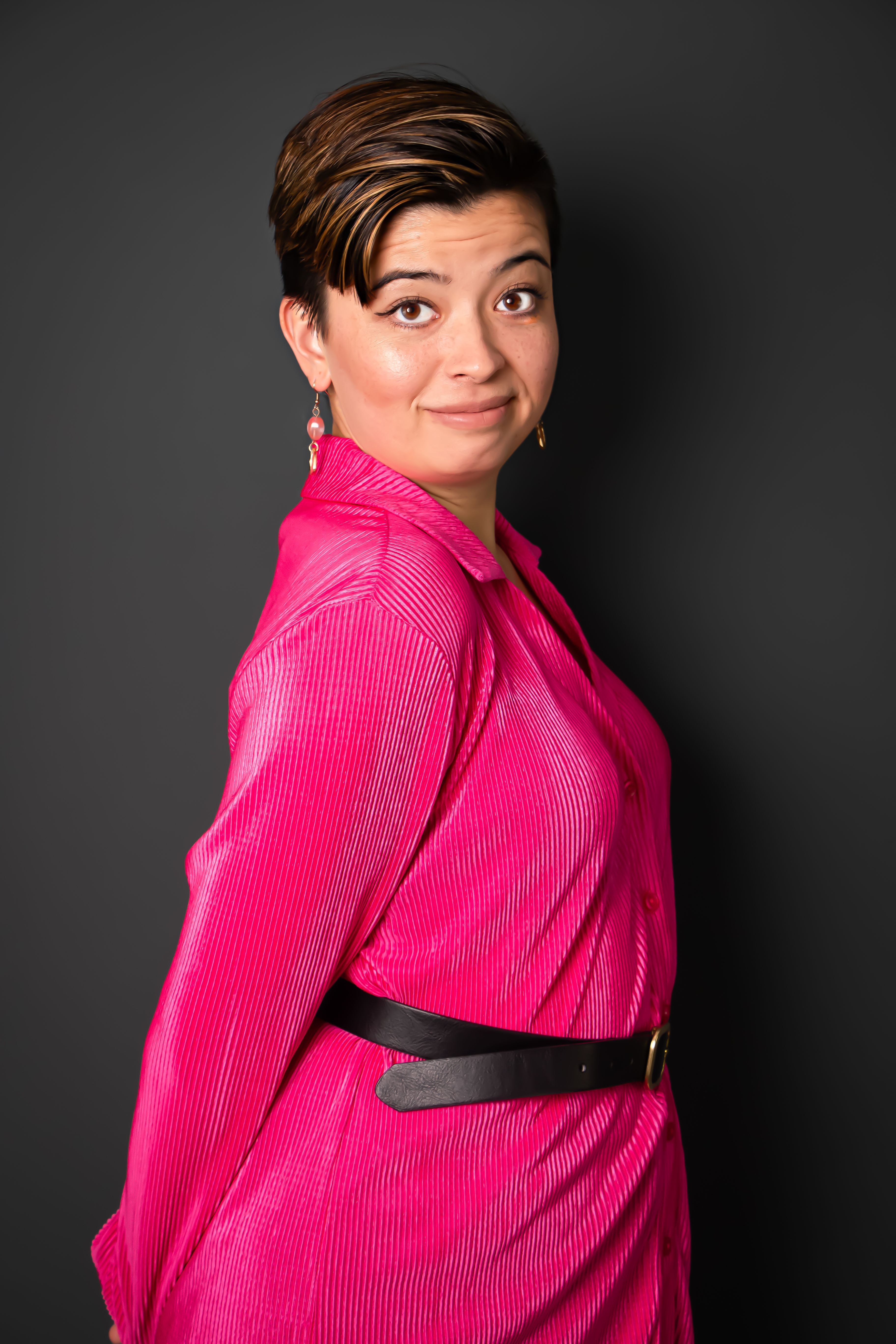 Studio portrait of a confident woman wearing a vibrant pink dress against a dark background.