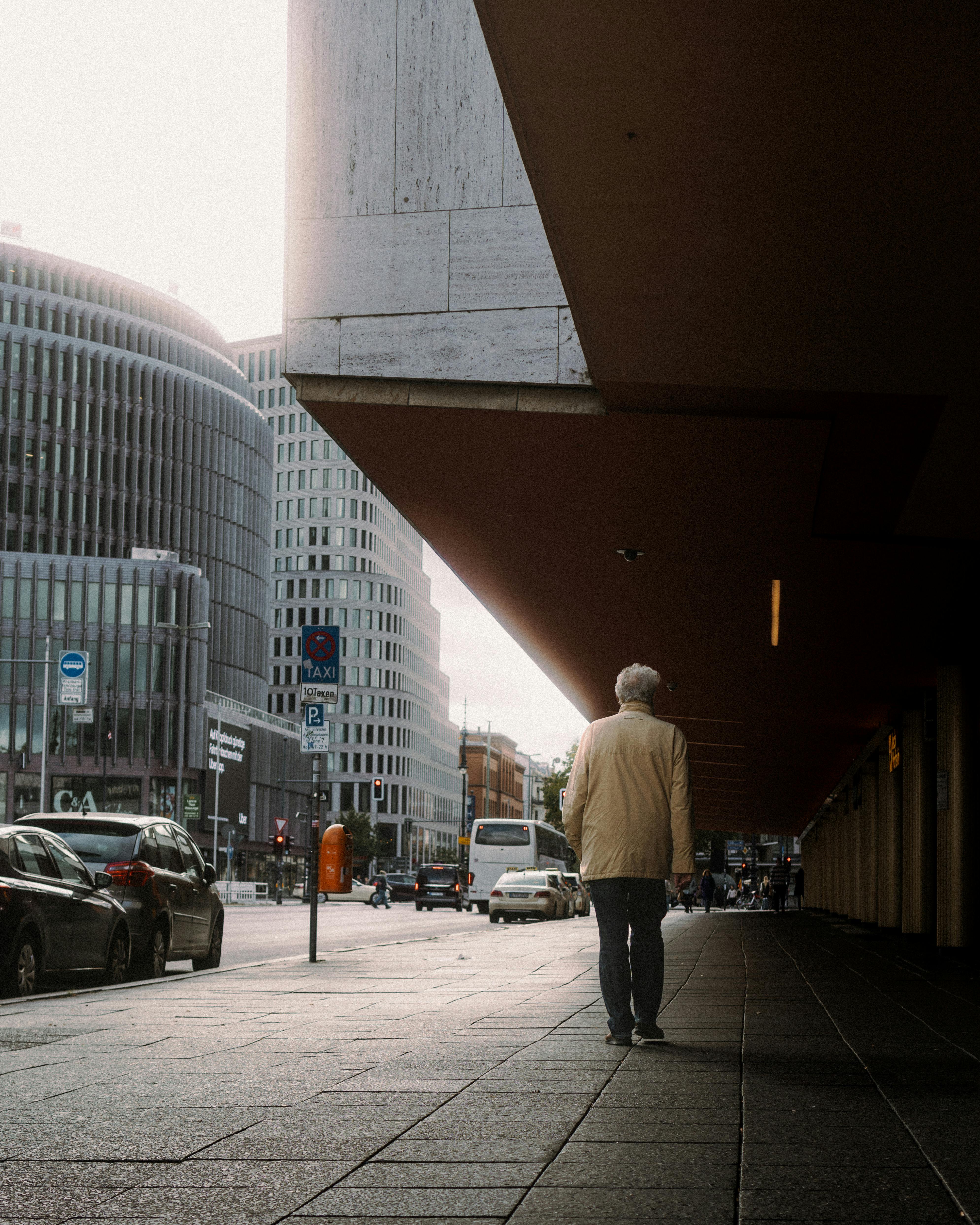 A senior man in a jacket walking along a busy city sidewalk in Berlin, Germany.