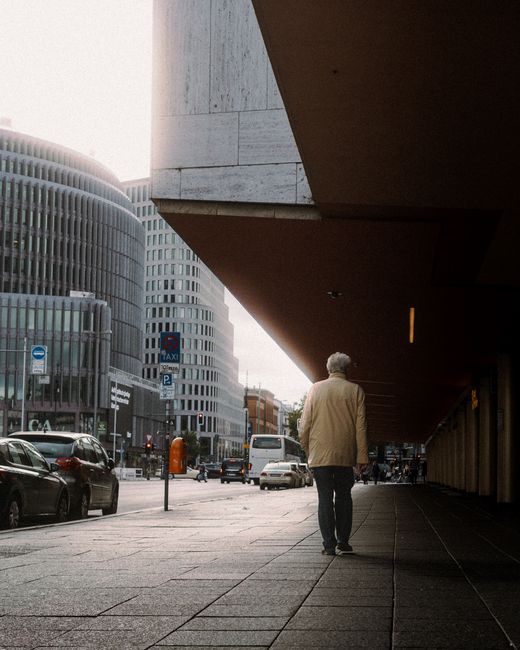 A senior man in a jacket walking along a busy city sidewalk in Berlin, Germany.