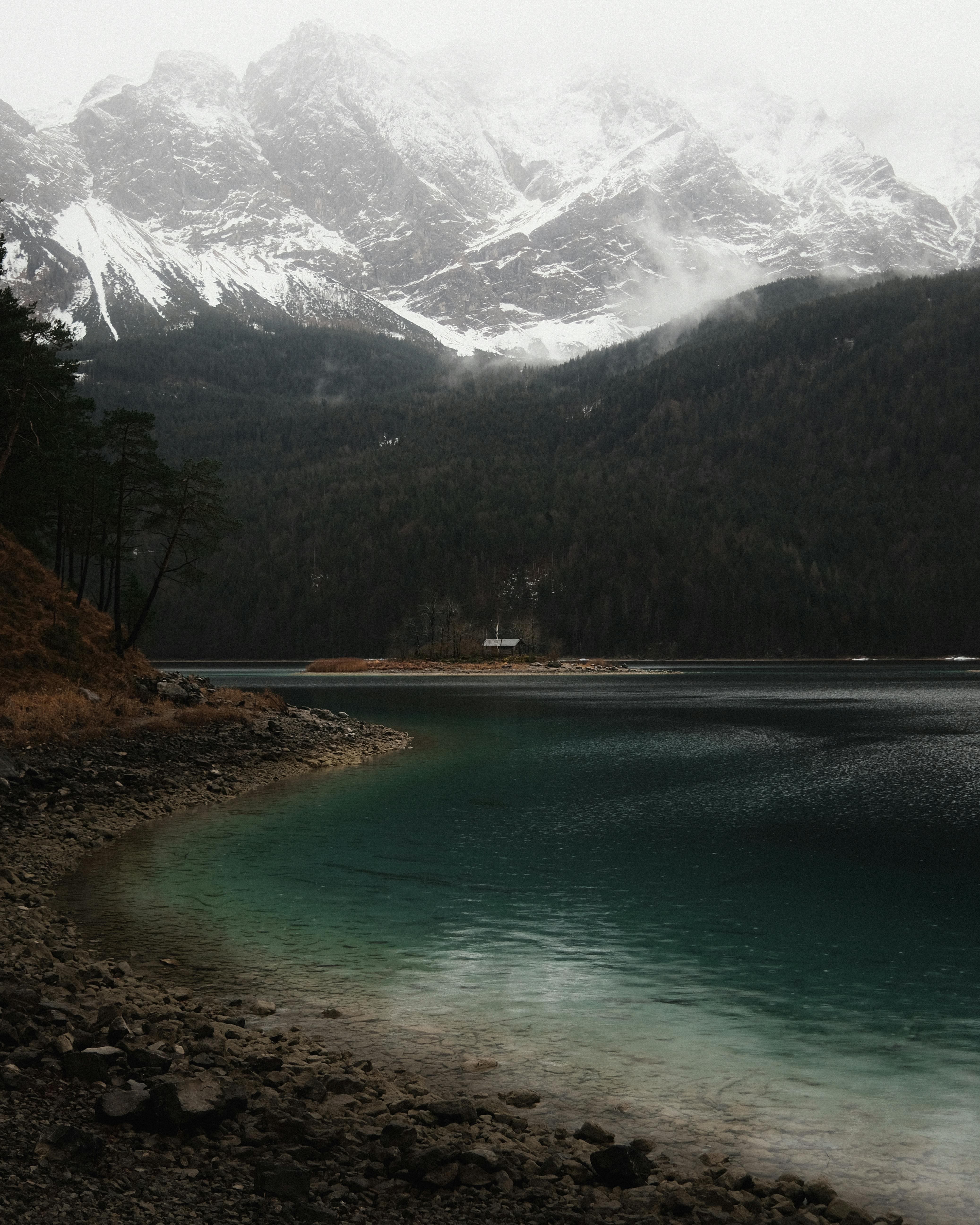 A serene alpine lake reflecting snow-covered mountains, surrounded by coniferous trees.