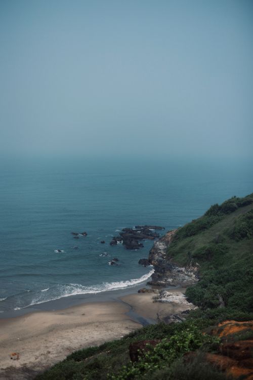 Free A serene aerial view of a coastline with rocky cliffs and a tranquil beach under a clear sky. Stock Photo