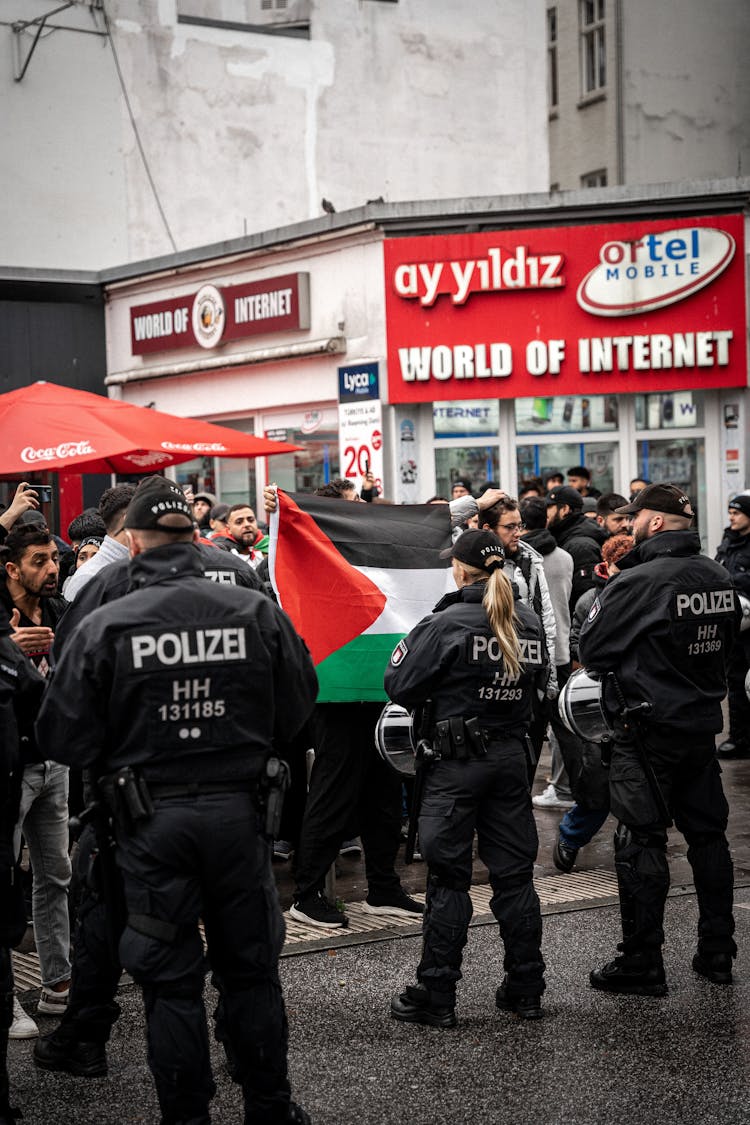 Police Standing In Front Of The Protestants With The Flag Of Palestine