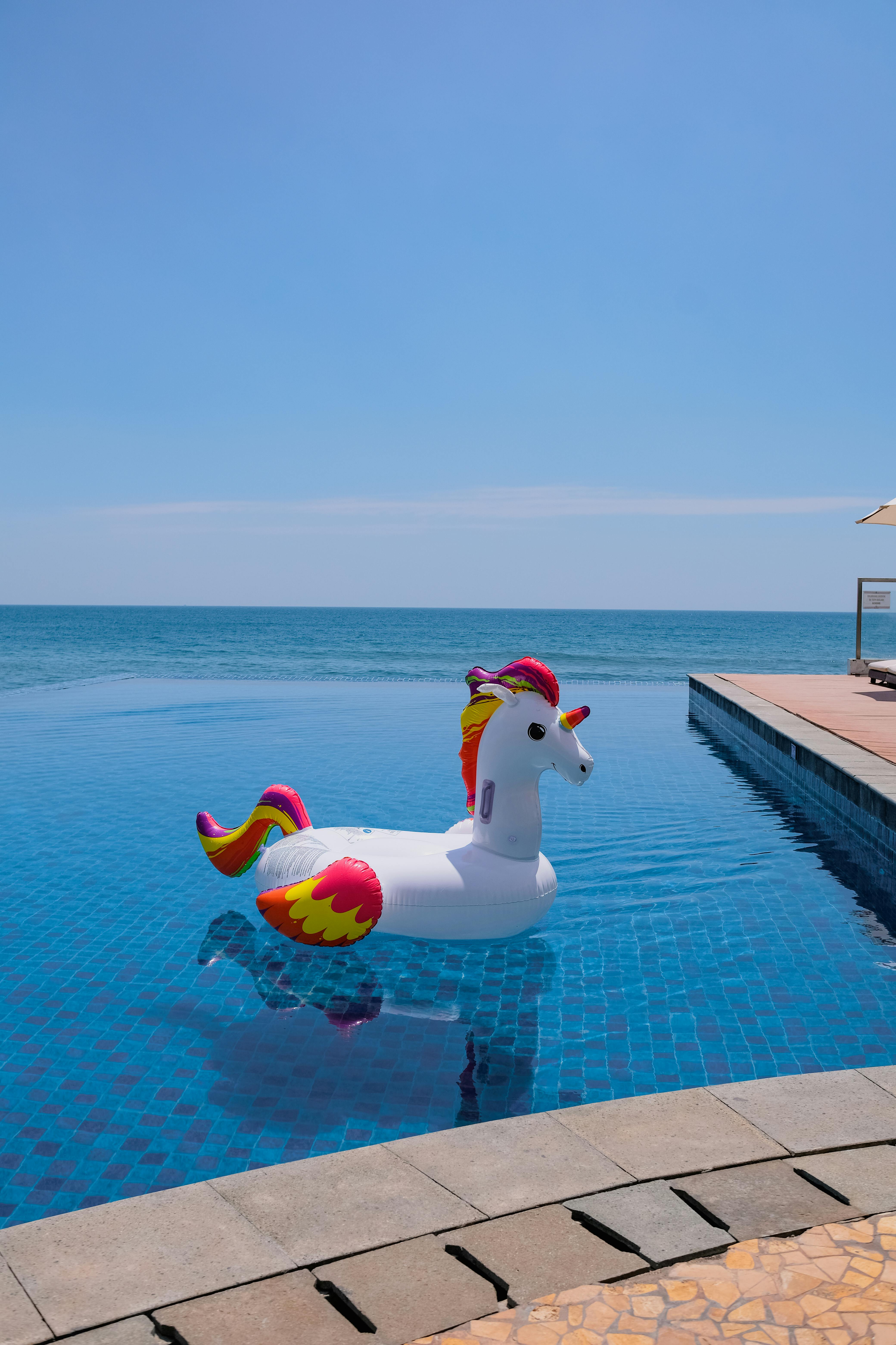 A vibrant unicorn inflatable in a serene infinity pool with a clear ocean view in Lamongan, Indonesia.