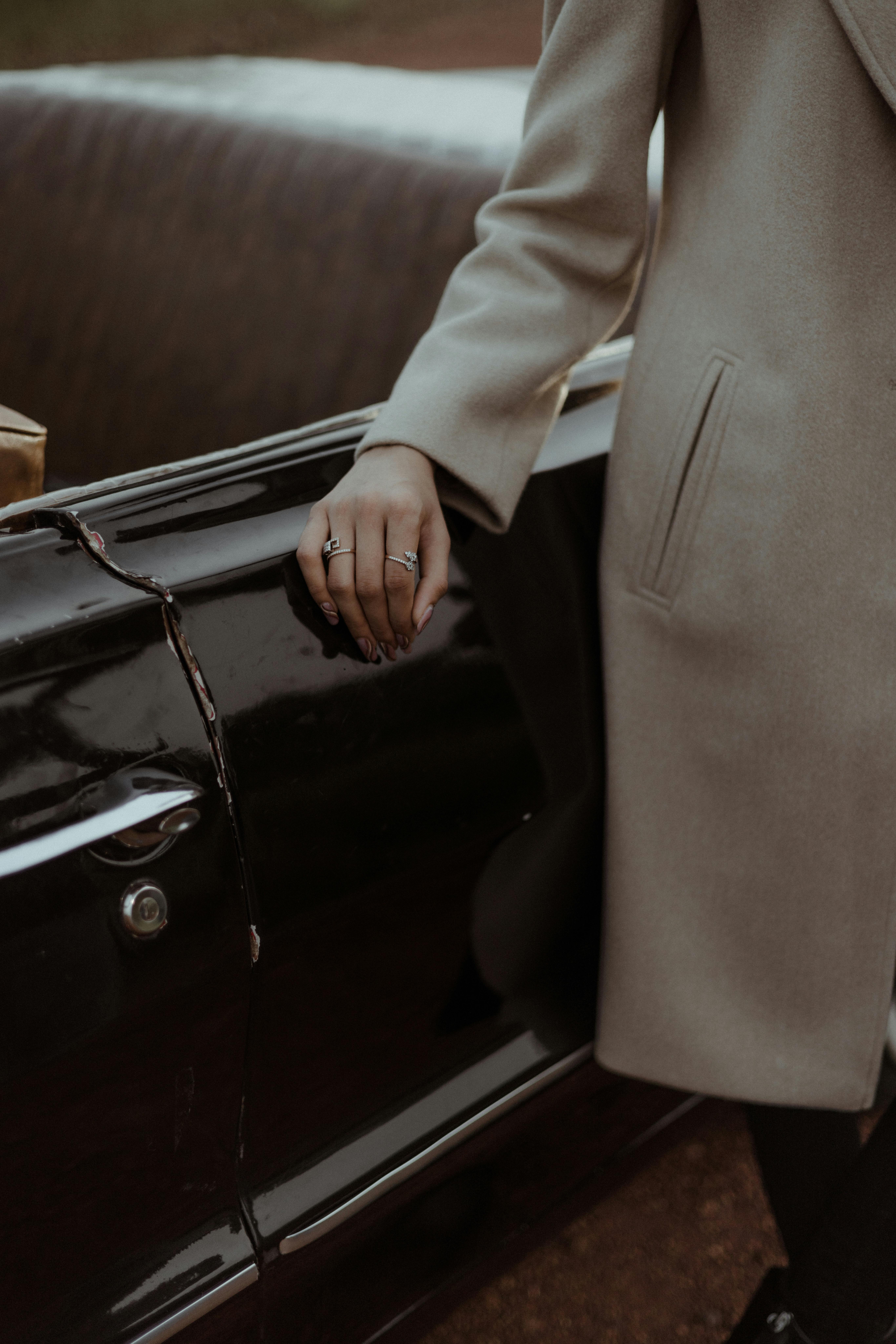 A person wearing a trench coat stands by a vintage convertible car, showcasing timeless elegance.