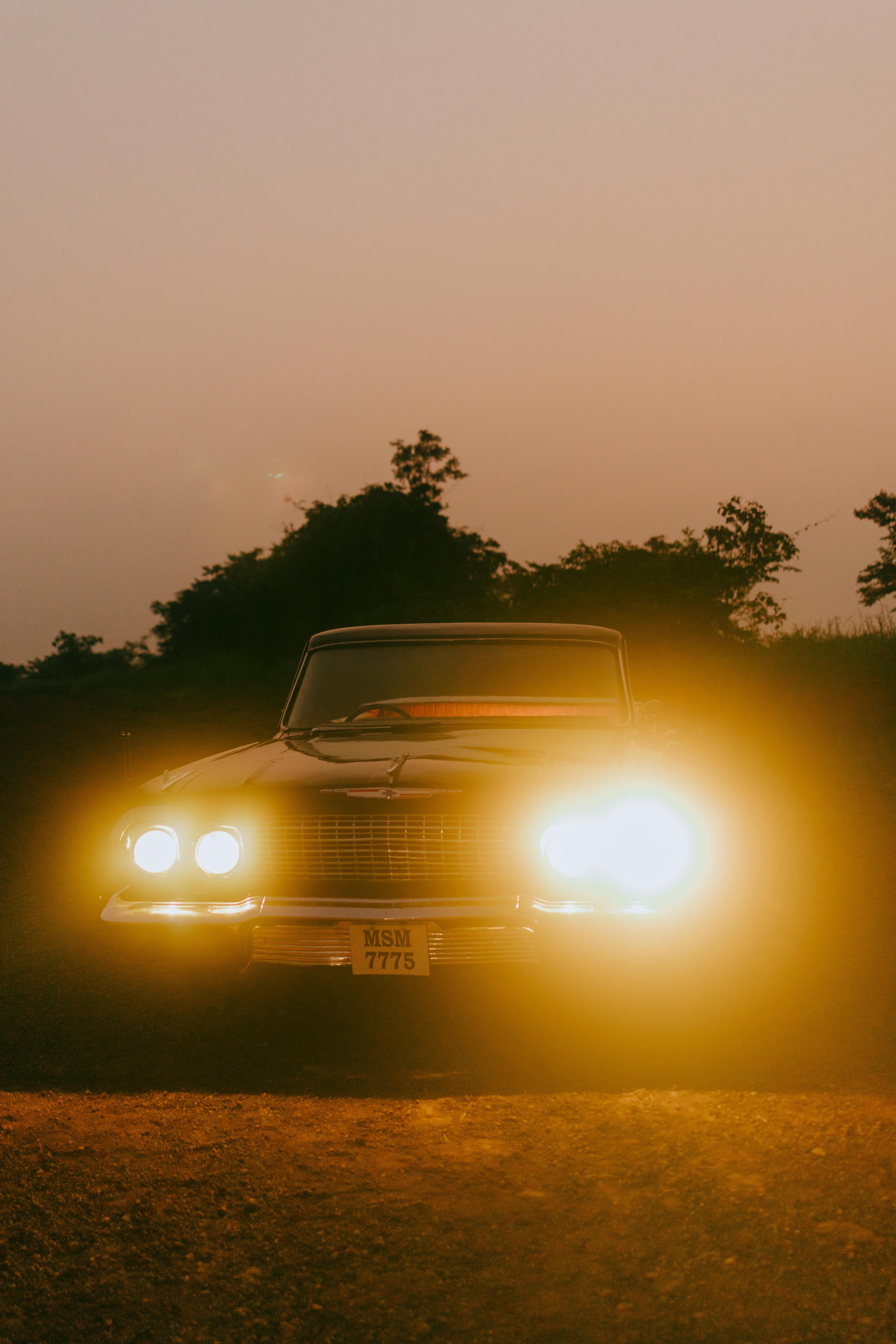 A vintage car with headlights on, captured during a moody, atmospheric dusk setting.