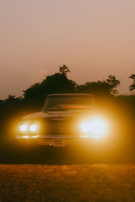 A vintage car with headlights on, captured during a moody, atmospheric dusk setting.