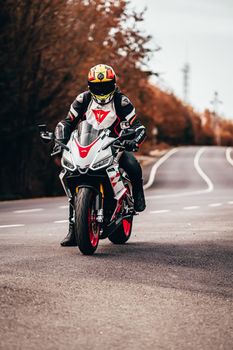 A motorcyclist in full gear riding on an empty autumn road, showcasing speed and adventure.