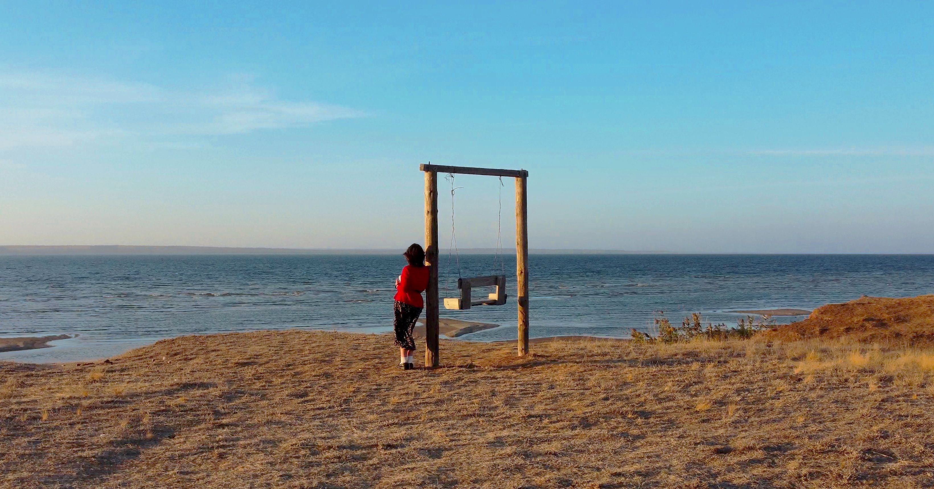 Woman relaxing by the ocean on a swing, capturing a serene evening atmosphere.