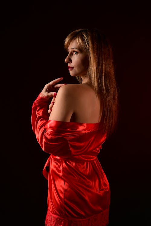 Photo of a Woman Posing in a Red Silky Dress against Black Background