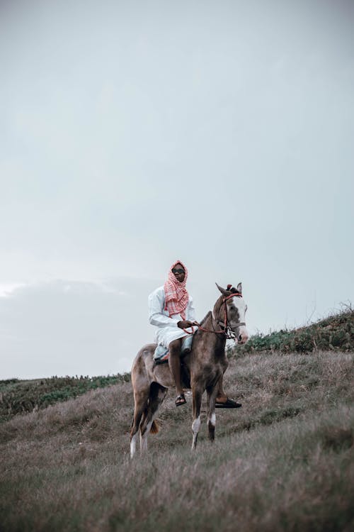 Man in Kufiyya Scarf and White Jalabiya Tunic Sitting on a Horse