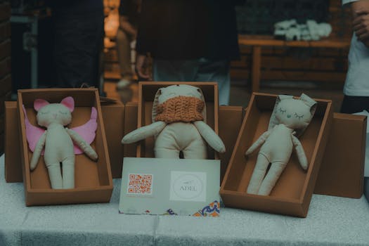 A close-up of handmade plush toys in cardboard boxes displayed indoors at a craft event.