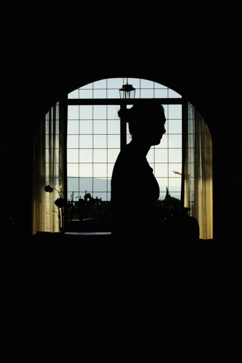 Free Elegant silhouette of a woman by a large window, backlit by twilight. Stock Photo
