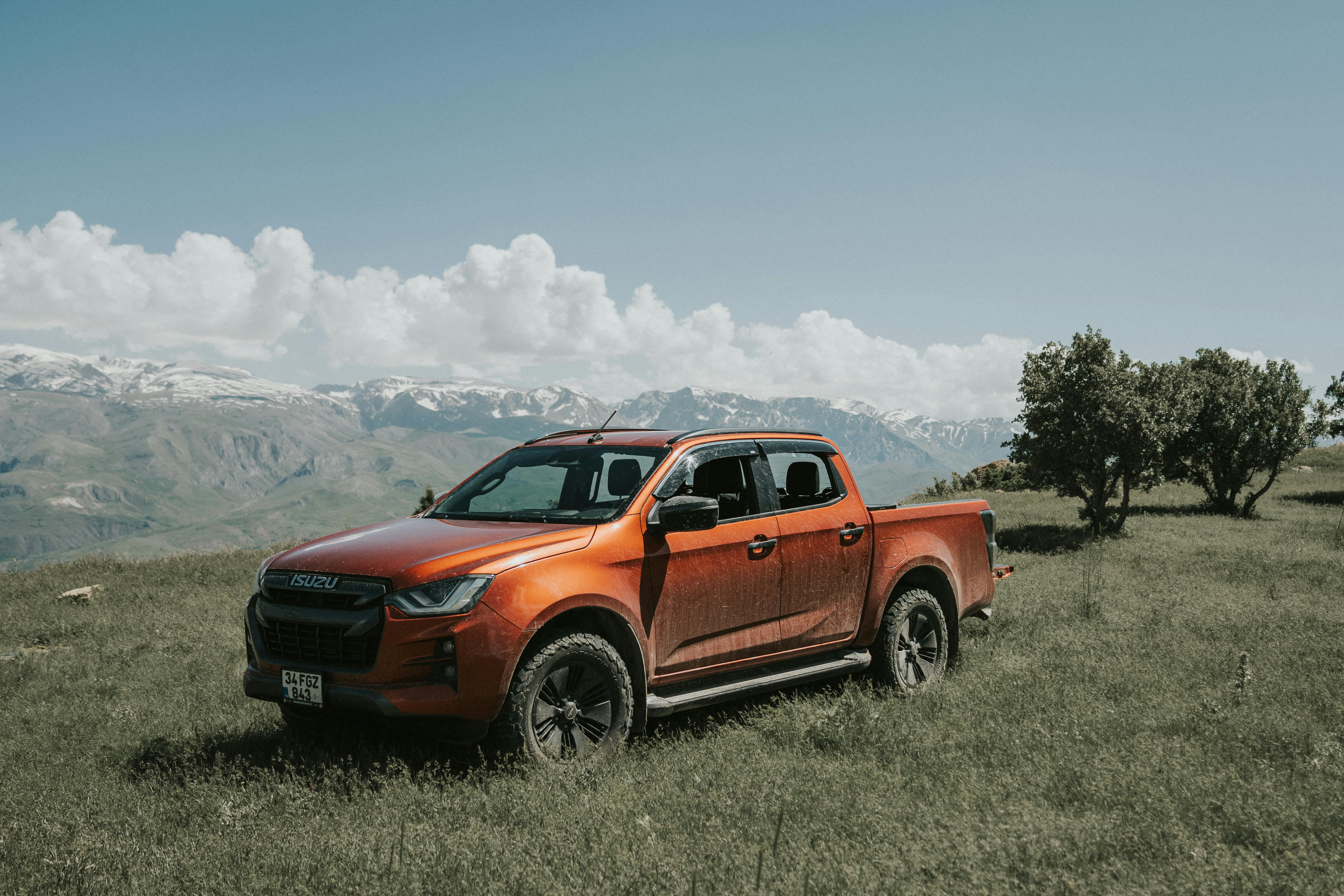 Orange pickup truck in scenic Erzincan mountains against clear sky and open field.