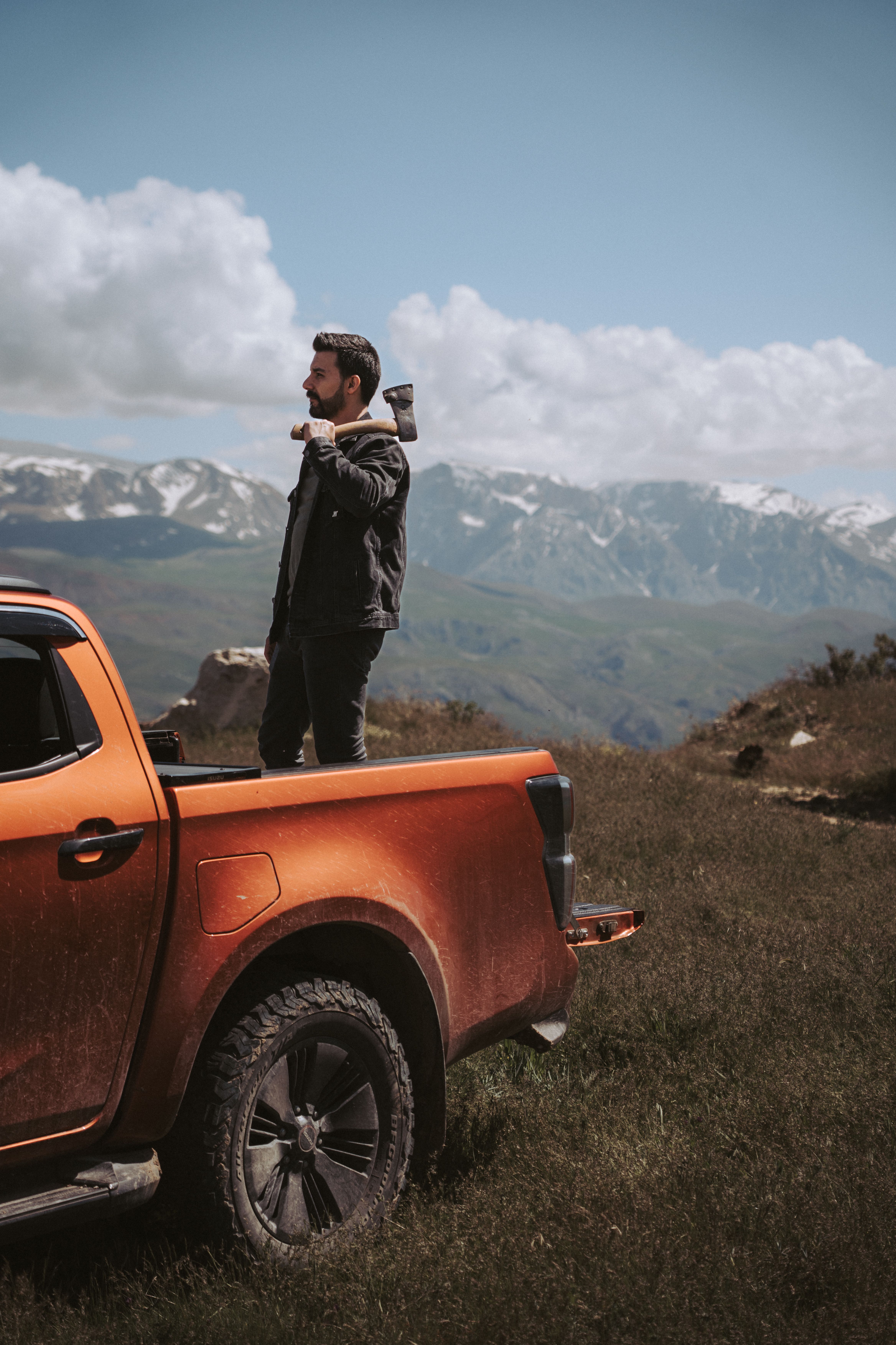 Man holding an axe standing by an orange truck in a scenic mountainous landscape.