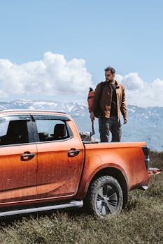 Adventure seeker standing by a pickup truck against a scenic mountain backdrop.