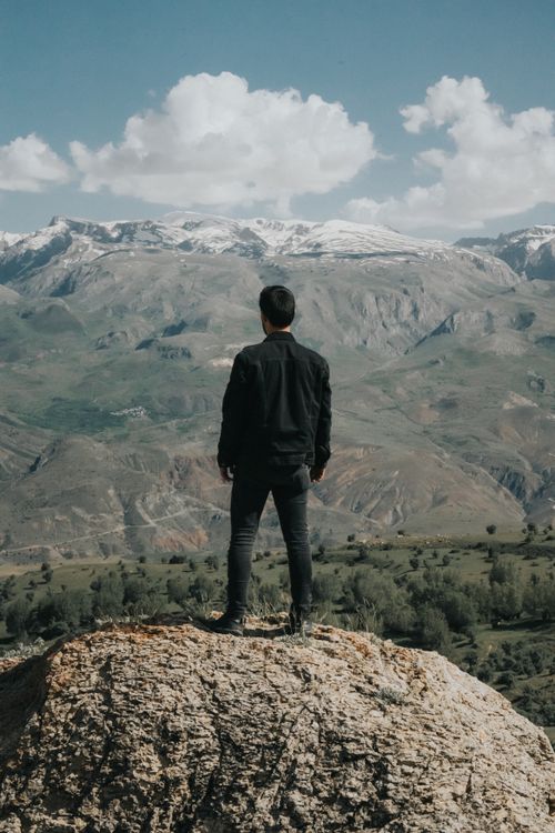 Free A man stands on a rock gazing at a vast mountain range, capturing the essence of nature and solitude. Stock Photo