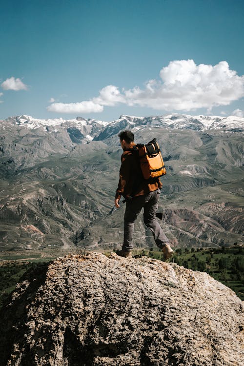 Hiker with Backpack Standing on Boulder in Mountains