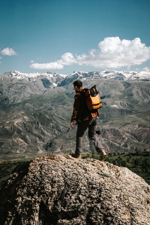 Free Man with backpack hiking on a rocky mountain summit against a stunning landscape. Stock Photo