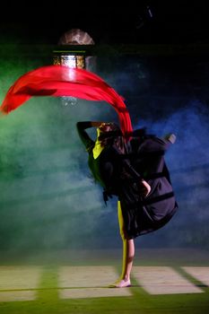 Ballet dancer in dramatic pose with flowing red cloth against smoky background.