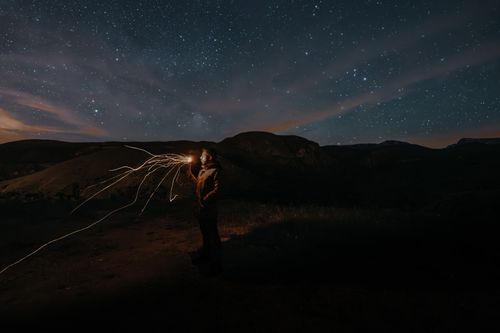 Free A person standing on a hill at night, creating light trails under a vast starry sky. Stock Photo