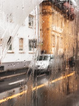 View through a raindrop-covered window onto a rainy city street with buildings.