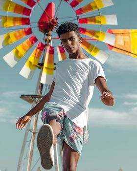 Stylish man posing confidently in front of a vibrant windmill on a sunny day.