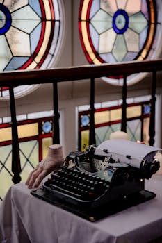 A vintage typewriter and mannequin hand in front of colorful stained glass windows.