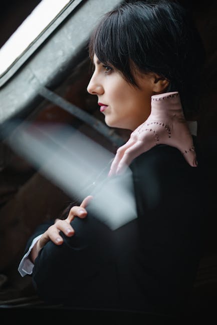 A woman in black with a pale hand on her shoulder gazes out a window.
