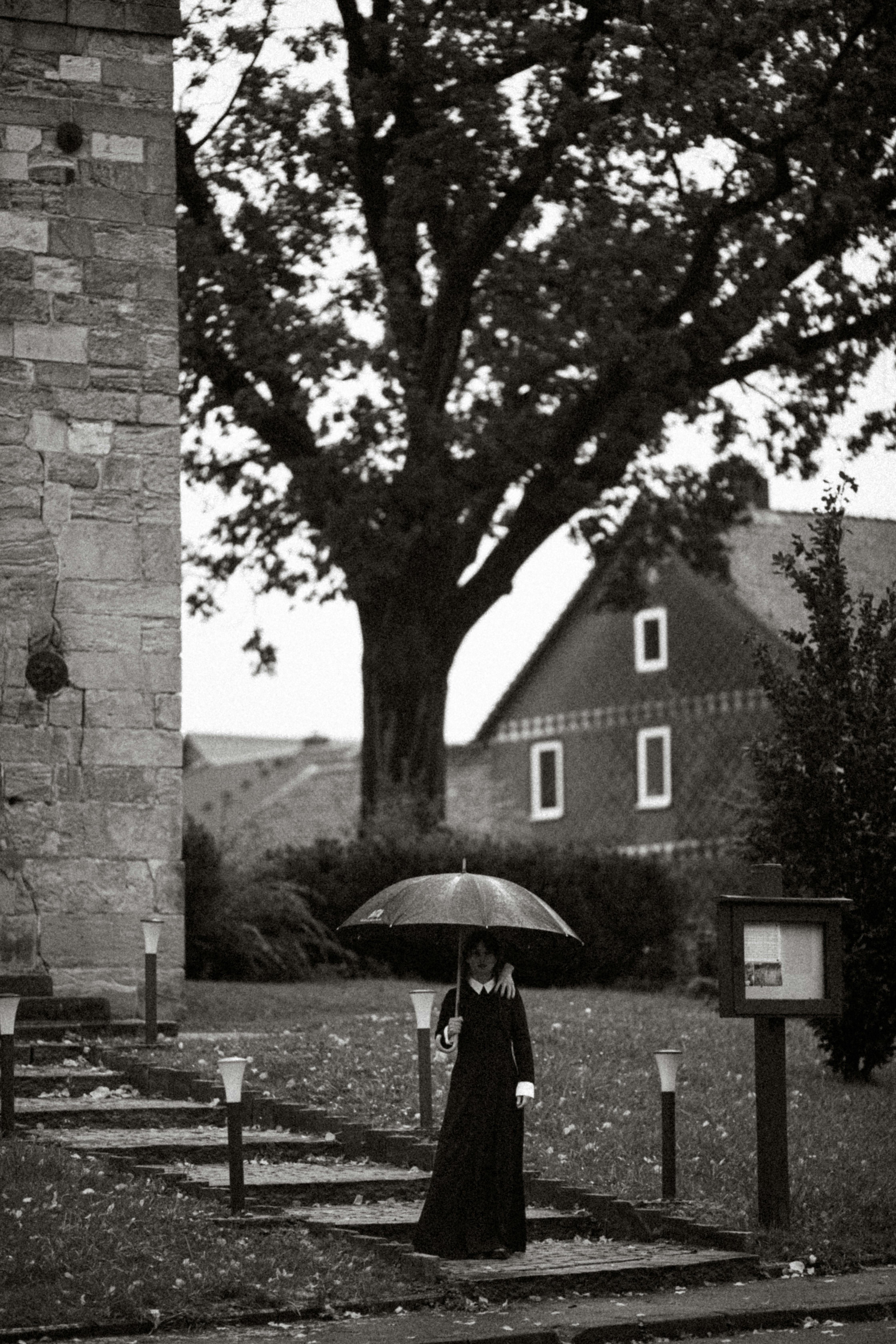 Gothic woman walking with umbrella in a spooky, eerie outdoor setting.