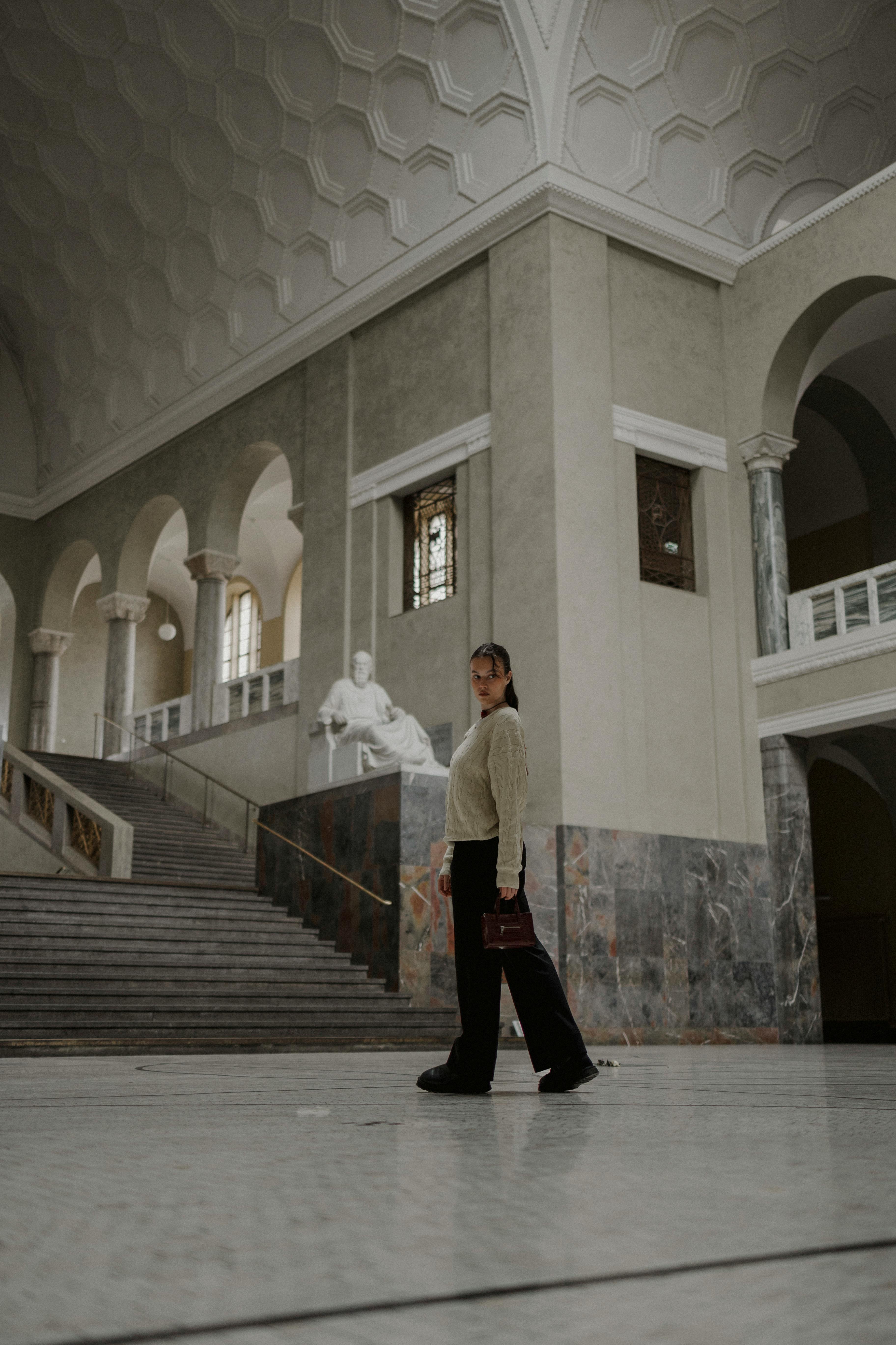 Teenager walking in a luxurious, historic lobby with statues and grand staircase.