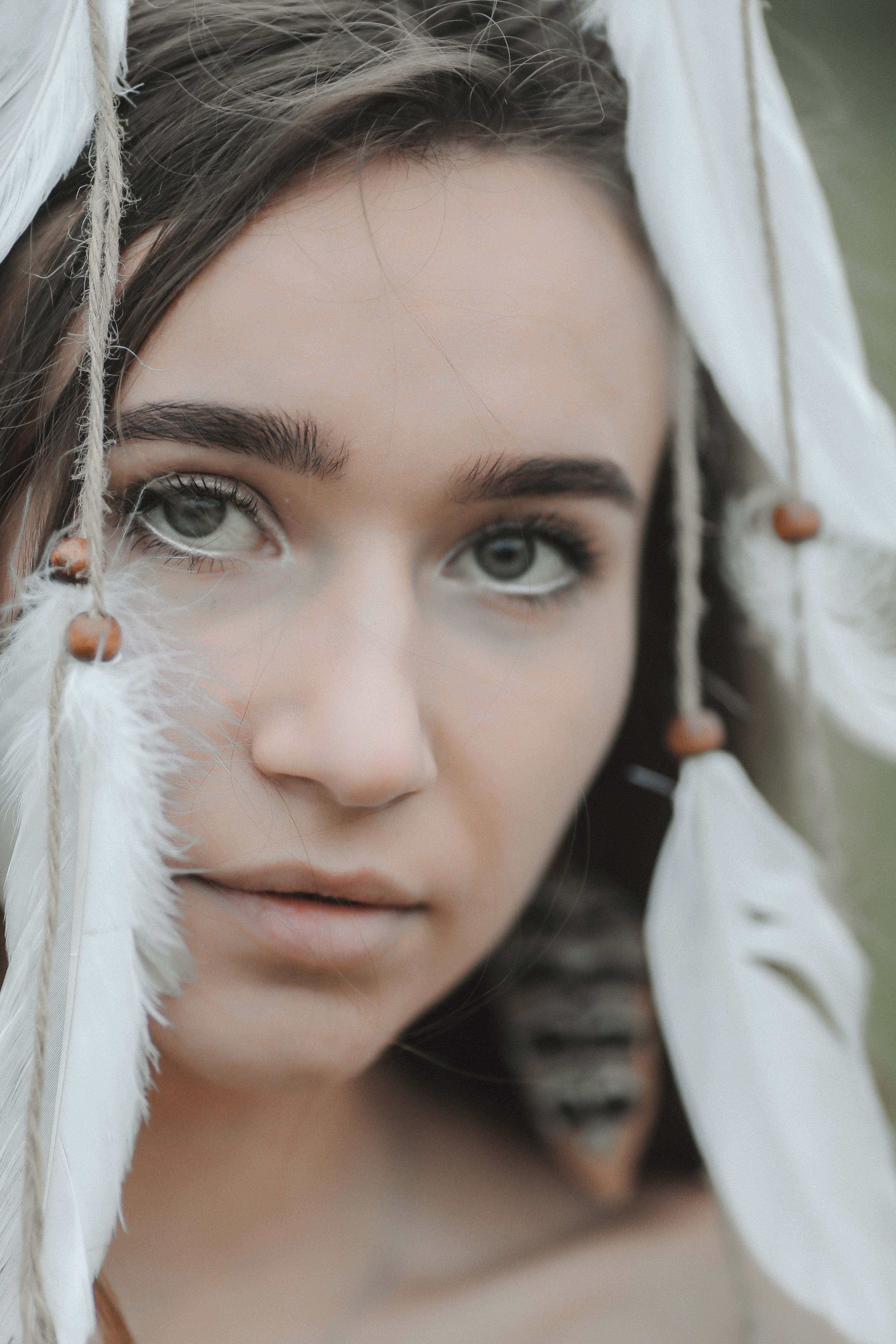 Serene close-up of a woman's face adorned with feathers, capturing a natural and artistic essence.