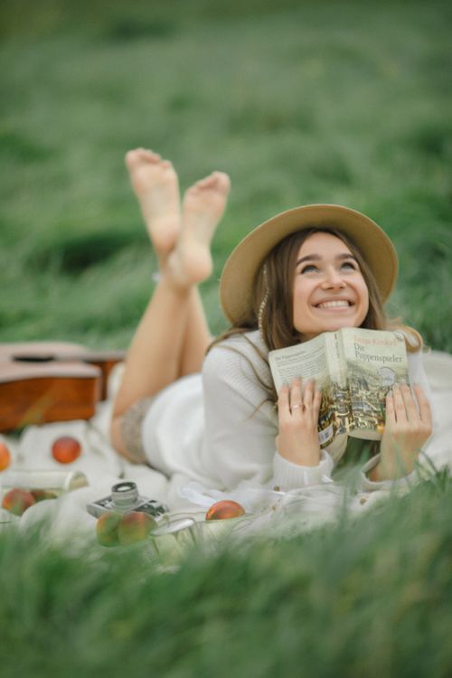 Free Joyful woman reading a book in a grassy field, surrounded by picnic elements. Stock Photo