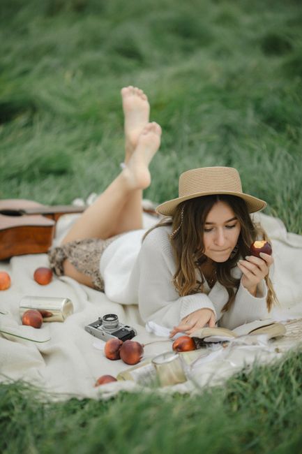Woman enjoying a picnic on grass with peaches and a vintage camera.